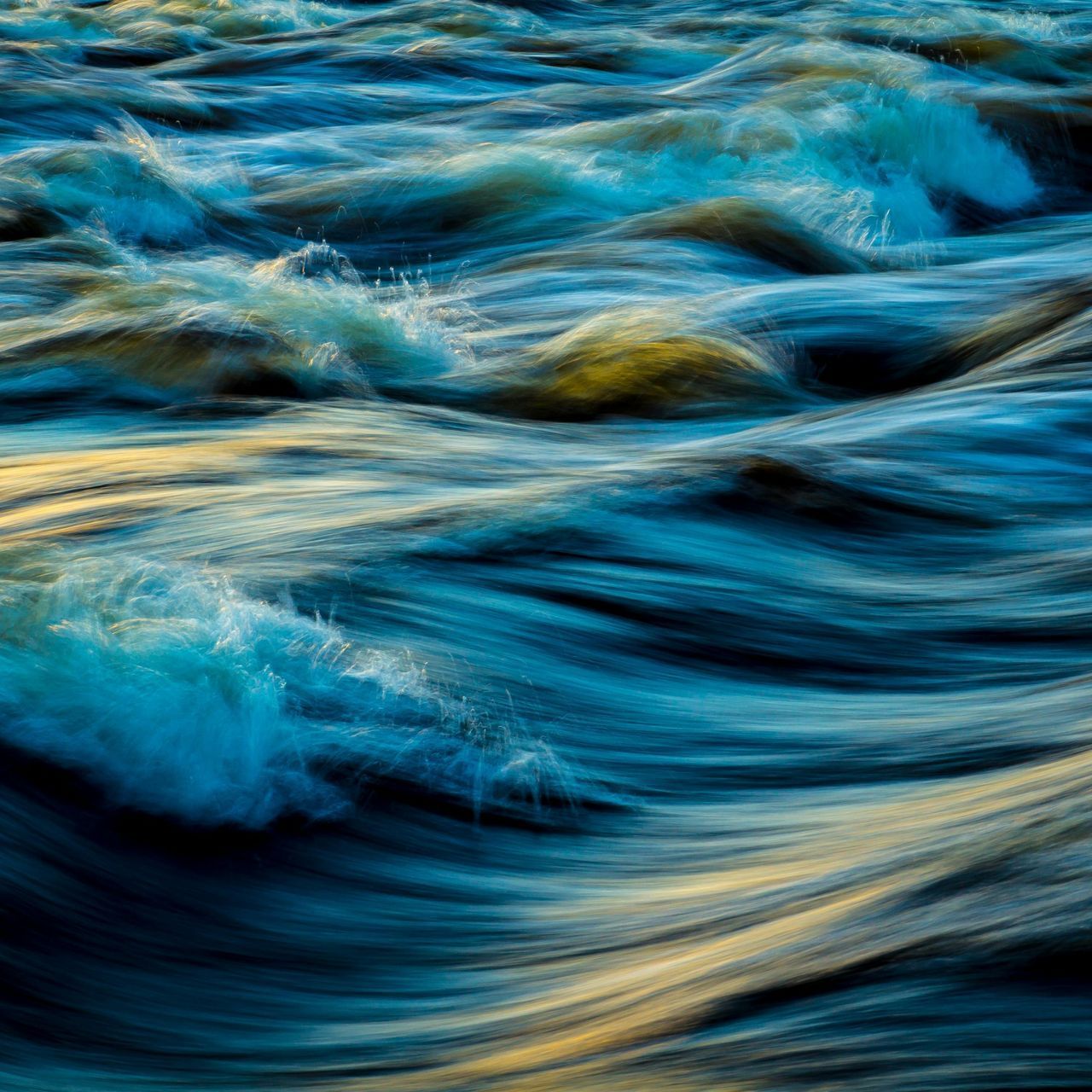Turbulent water, shades of blue and gold, captured with motion blur, creating an abstract, flowing effect.