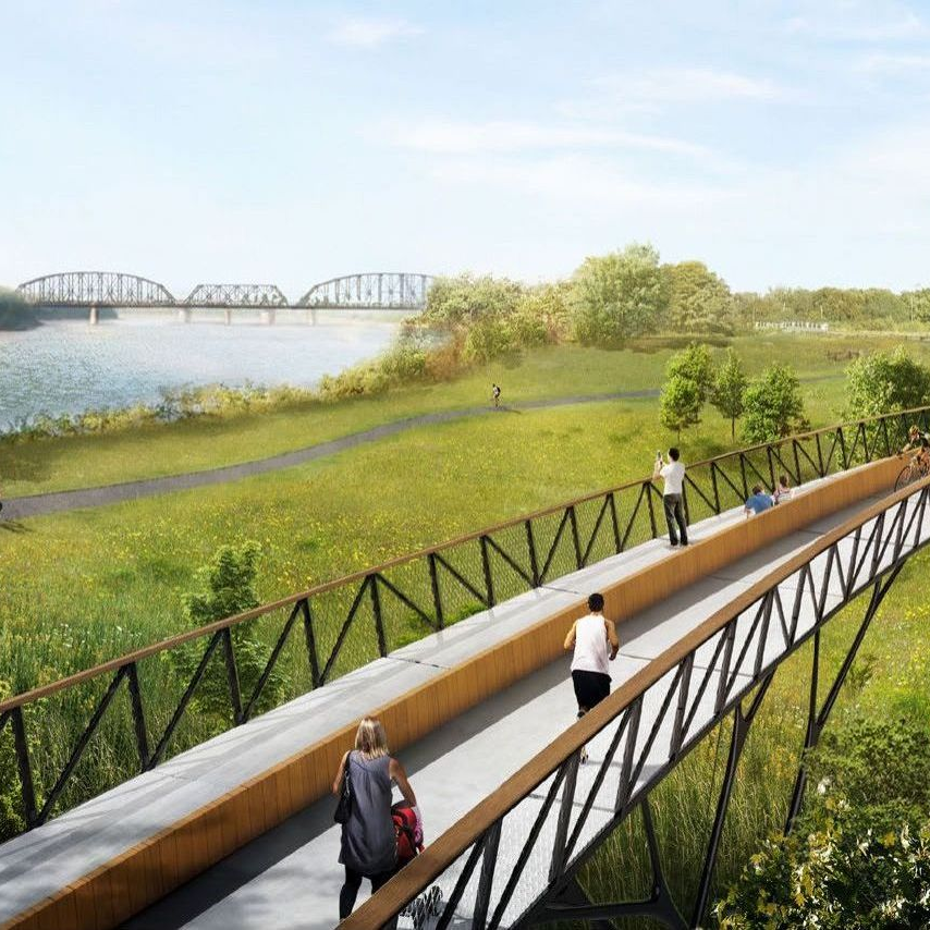 A walking bridge over a green landscape with people on it, next to a lake with a bridge in the background.