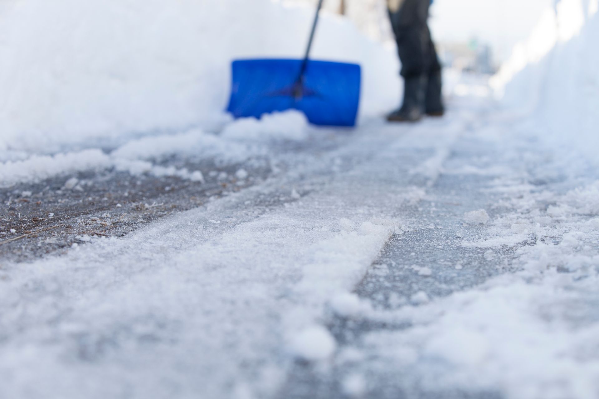 A Person Is Shoveling Snow from The Sidewalk with A Blue Shovel | Onalaska, WI | River City Irrigation