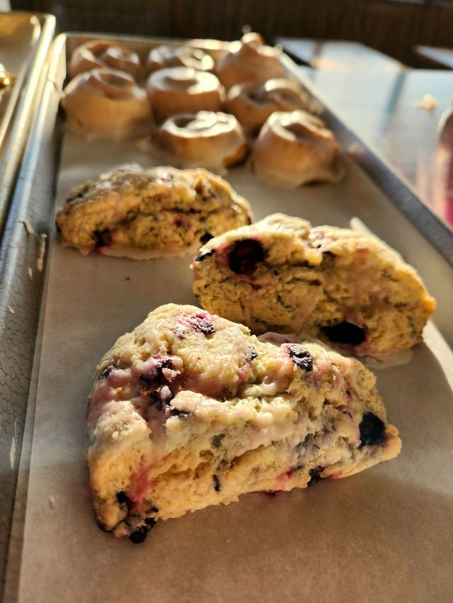 Fresh berry scones cooling on a baking tray in a kitchen, with one close in the foreground and more behind.
