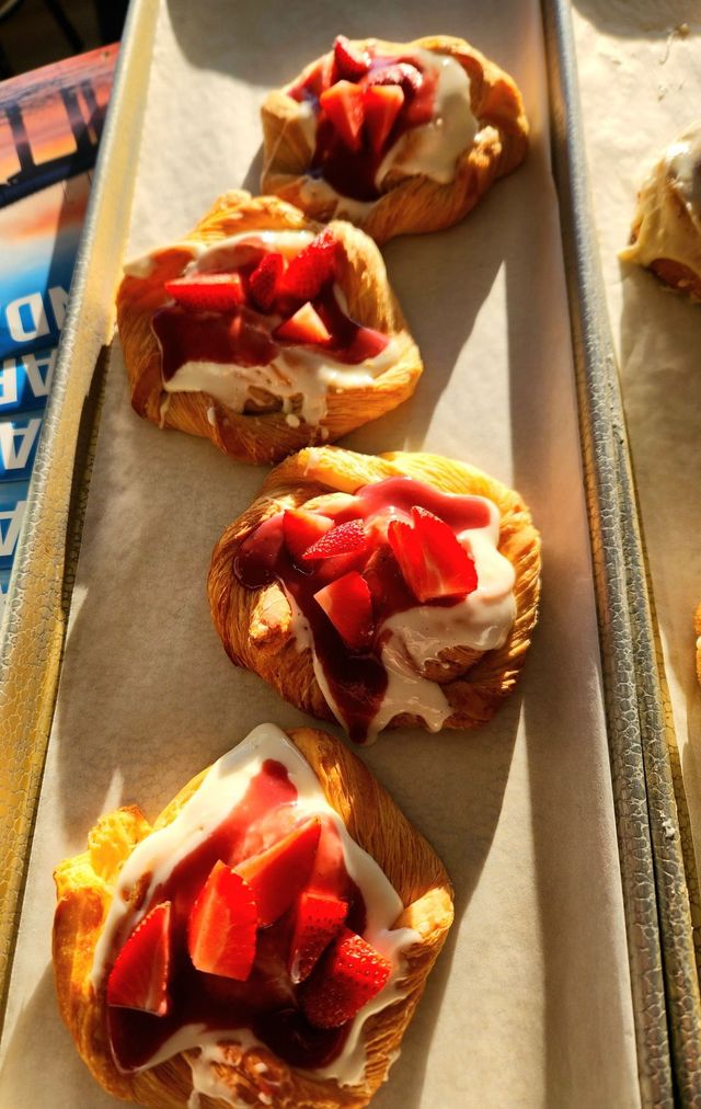 Strawberry-topped pastries arranged on a baking tray in warm light