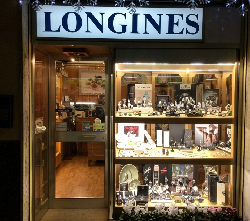 Facciata di un negozio di orologi Longines con vetrina illuminata e porta aperta.