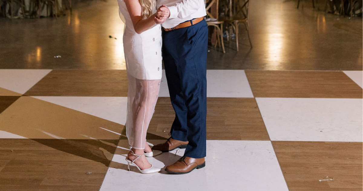 Two people dancing closely on a checkered floor, wearing white and blue outfits.