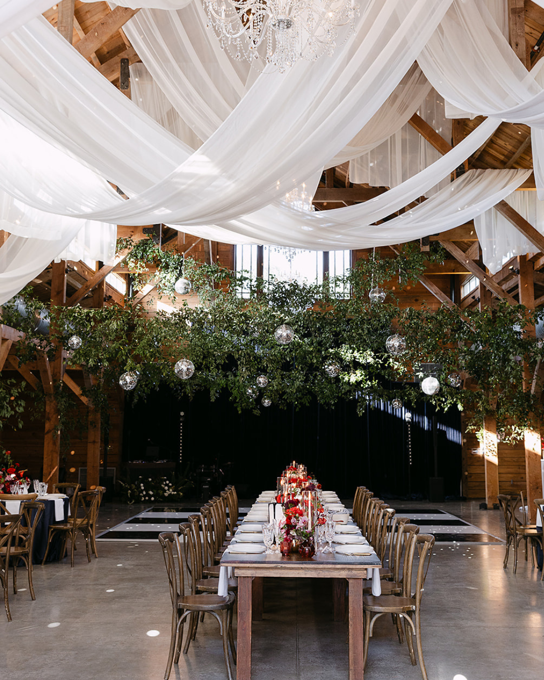 Rustic banquet hall with long table, floral centerpiece, and flowing white drapes overhead