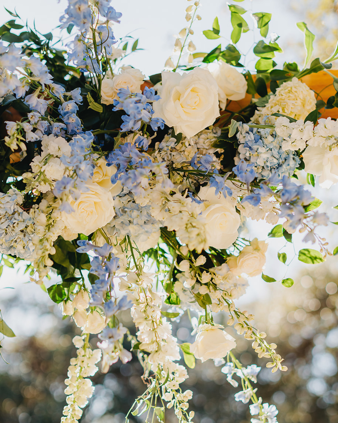 White and pale blue flowers with cascading greenery in a soft, airy floral arrangement