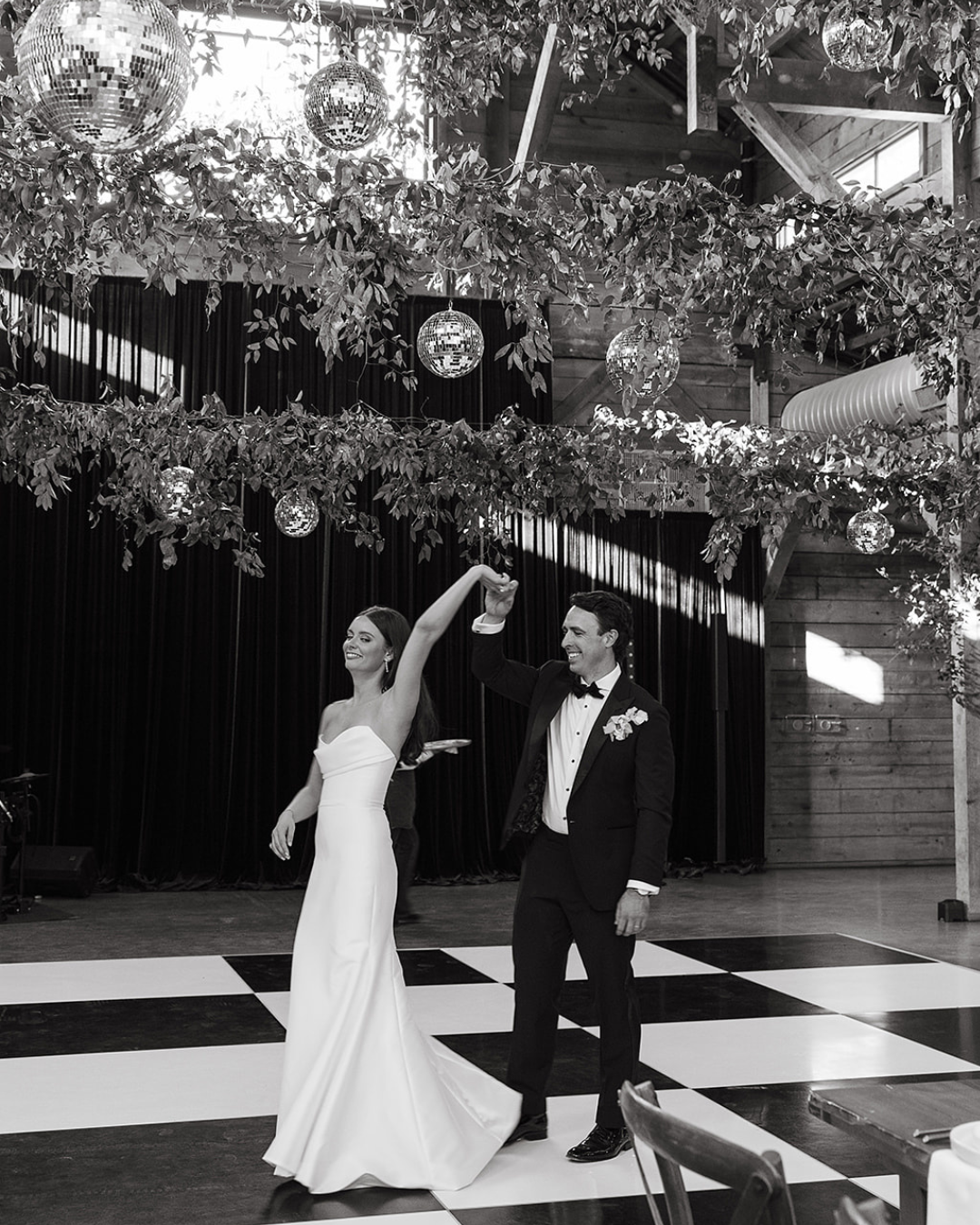 Bride and groom dancing under hanging greenery at an outdoor wedding reception