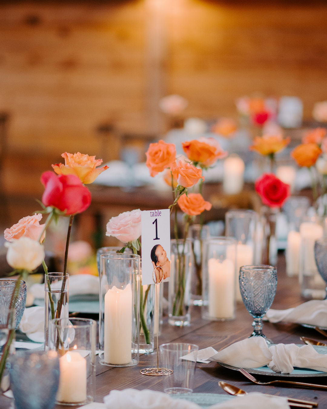 Elegant banquet table with candles, glass vases, and orange, pink, and red flowers