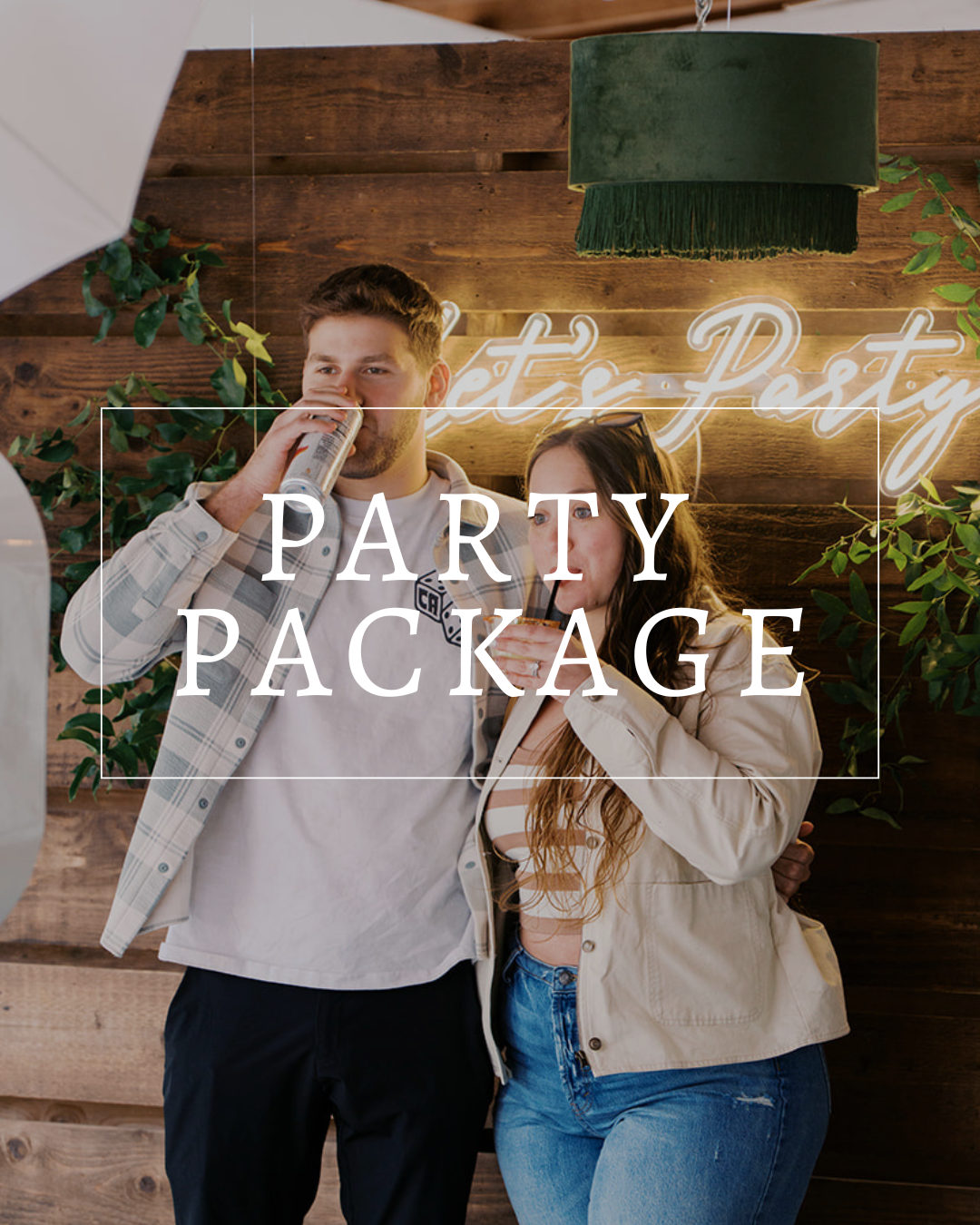 A man and woman drink from cans in front of a rustic wooden wall with a glowing