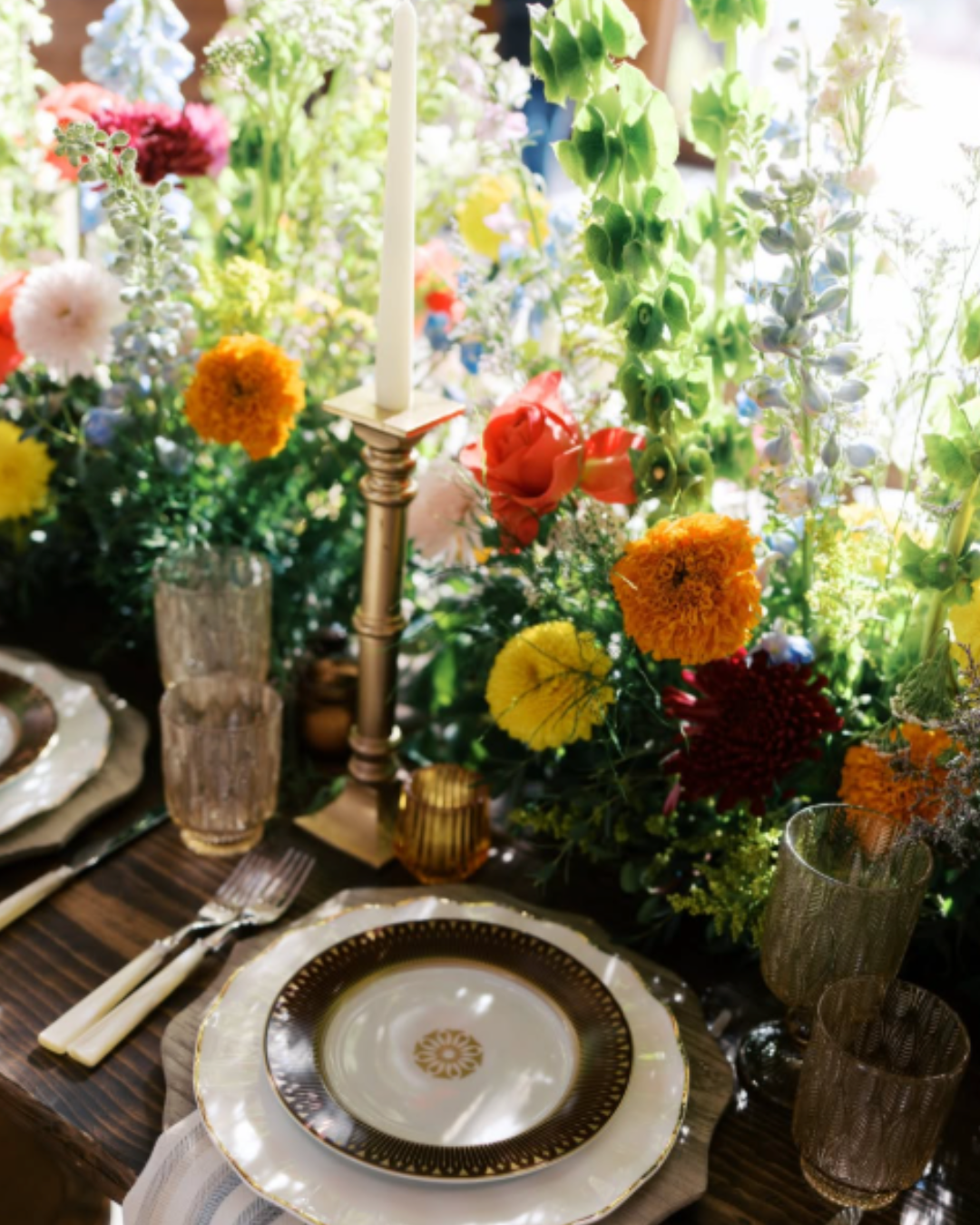 Elegant table setting with gold trim, candles, and colorful floral centerpiece by a bright window