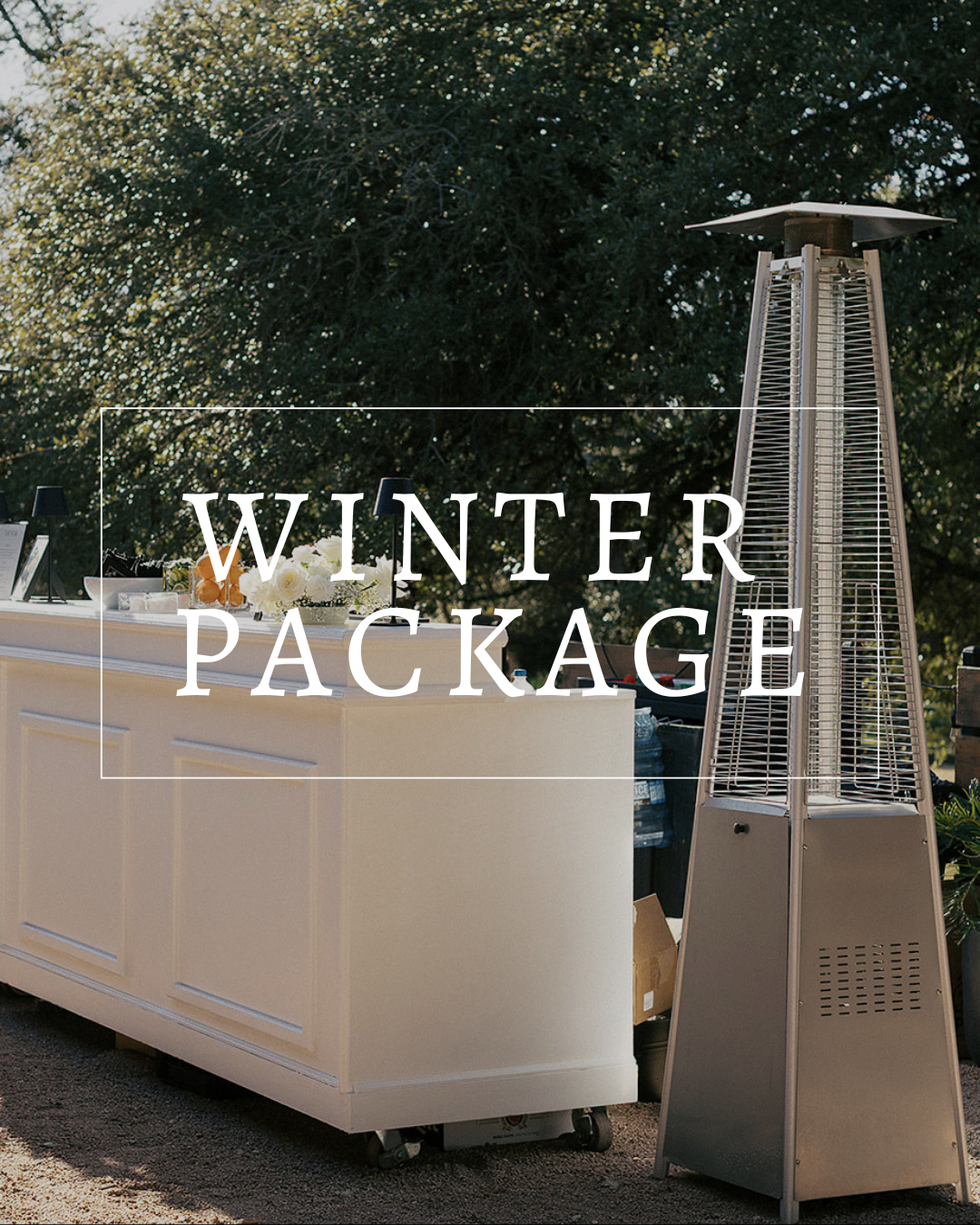 A tall outdoor patio heater stands next to a white bar on a gravel path, with