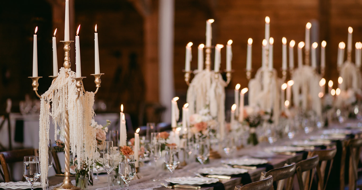 Elegant candlelit banquet table with white decor and tall candles in a softly lit room