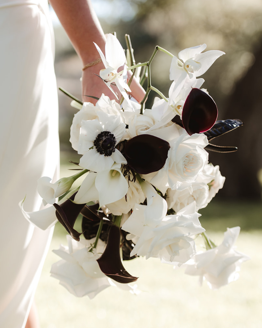 White and dark purple bridal bouquet held at a sunlit outdoor wedding