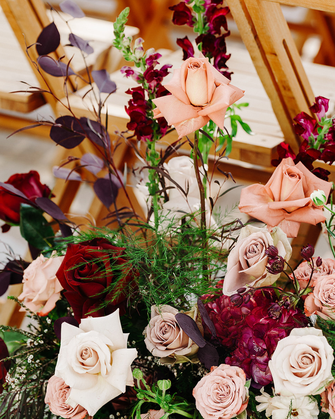 Assorted pastel roses and greenery arranged in a floral bouquet with soft pink, white, and burgundy blooms.