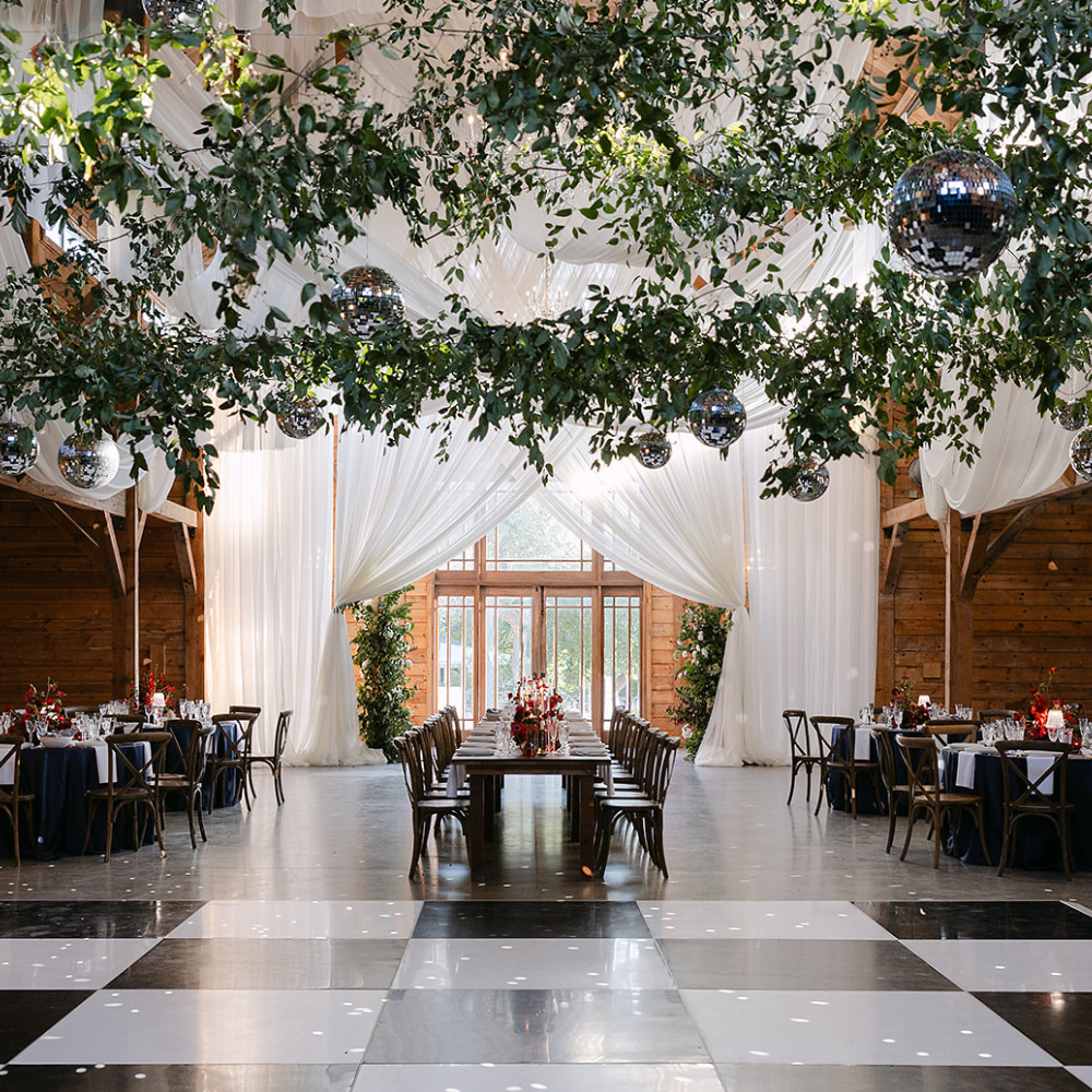 Elegant wedding reception hall with white drapes, greenery overhead, and black-and-white checkered floor