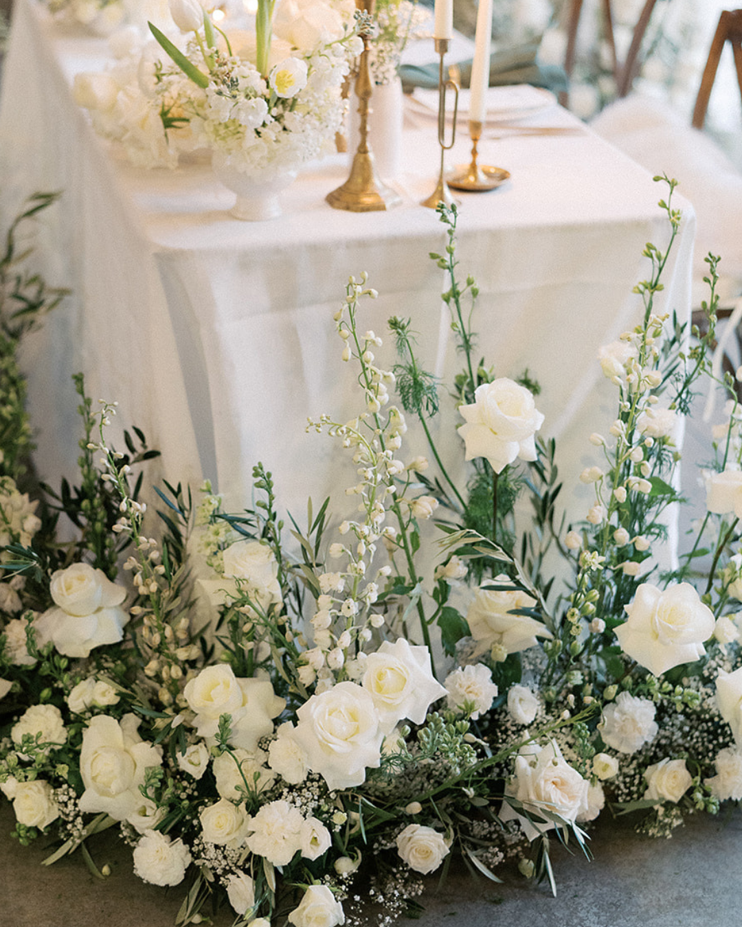 White floral wedding table centerpiece with greenery around a draped table and gold candle holders