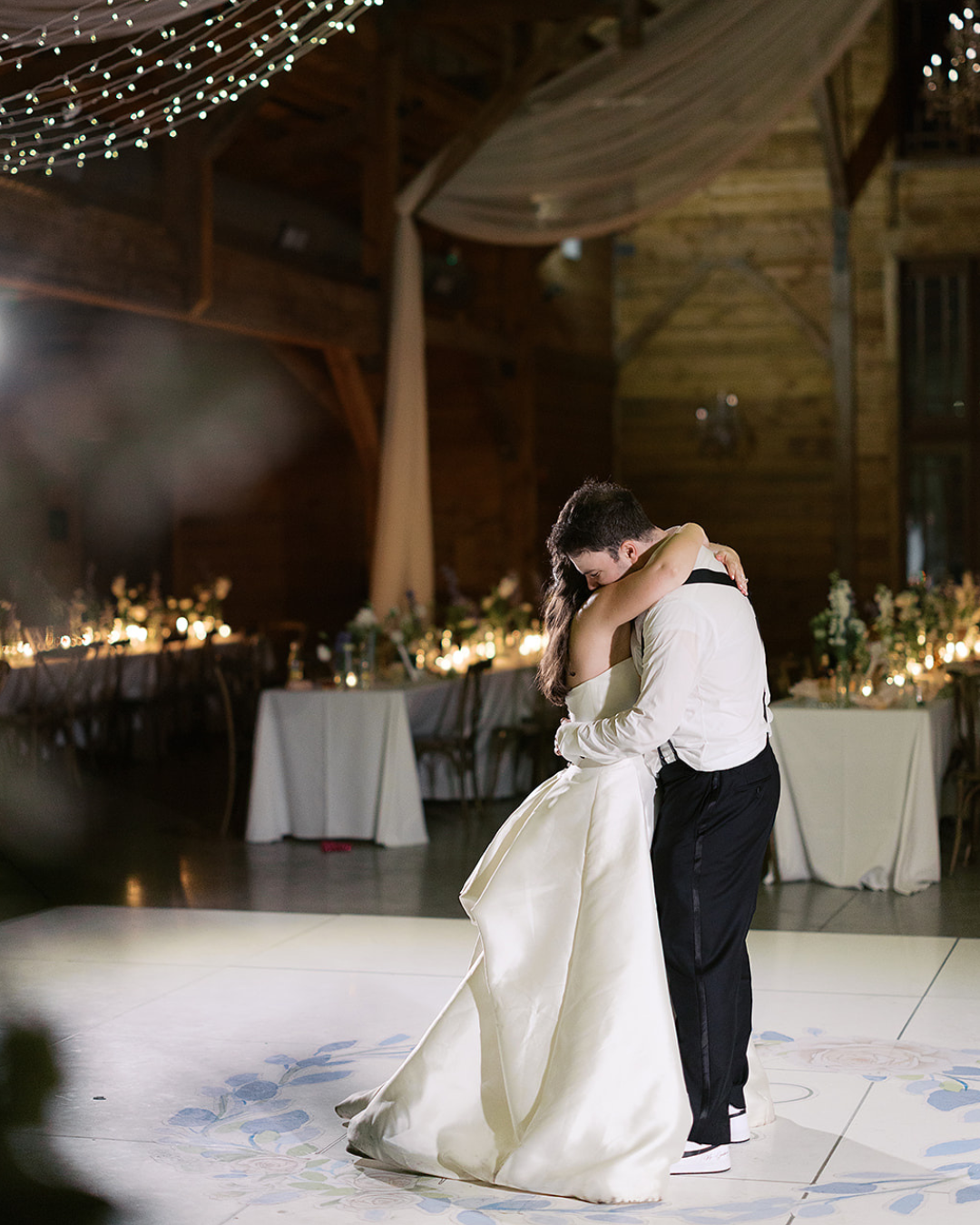 Bride and groom embracing during a first dance in a warmly lit rustic reception hall