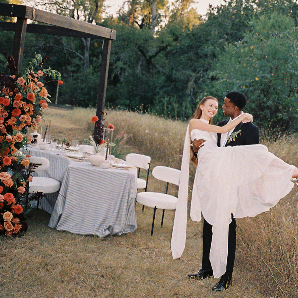 Couple dancing outdoors beside a decorated table and floral arch at a garden reception