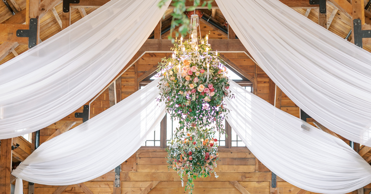 White draped fabric and a hanging floral arrangement decorate a rustic wooden wedding venue ceiling