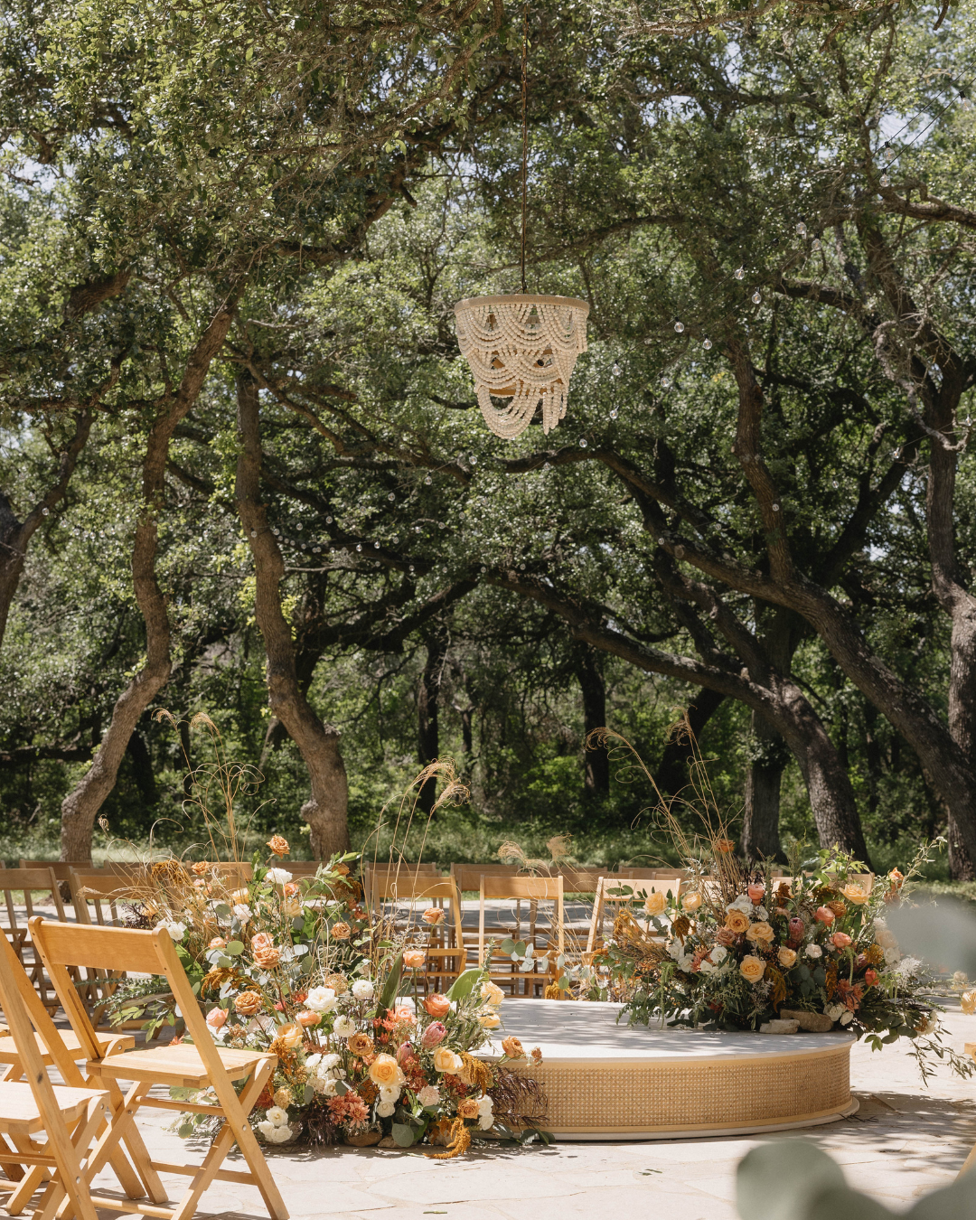 Outdoor wedding ceremony setup in the Texas Hill Country with a wooden arch decorated with flowers and rows of folding chairs under oak trees.