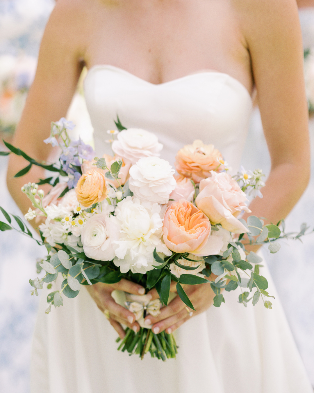 Bride holding a white, peach, and green wedding bouquet against a white dress