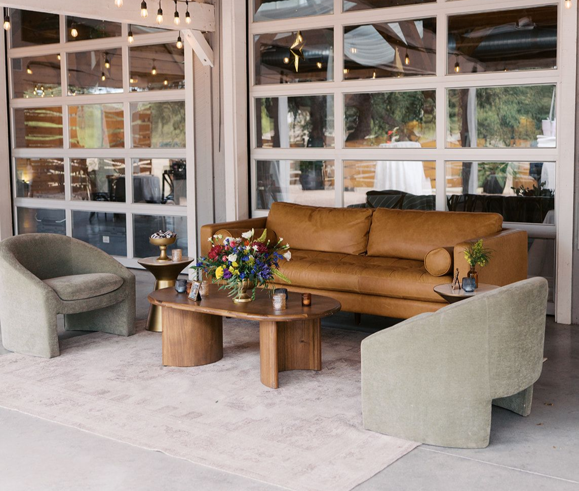 A tan leather sofa and two pale green chairs arranged around a wooden coffee table on a light-colored rug.