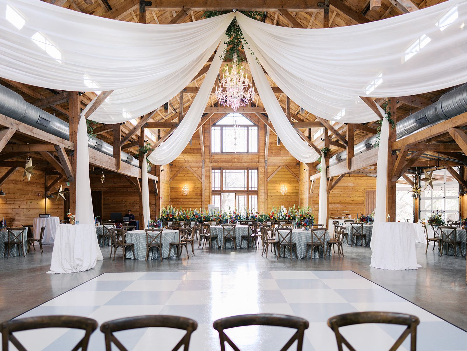 Rustic wedding venue with a white checkered dance floor, draped ceiling fabric, and wooden architecture.
