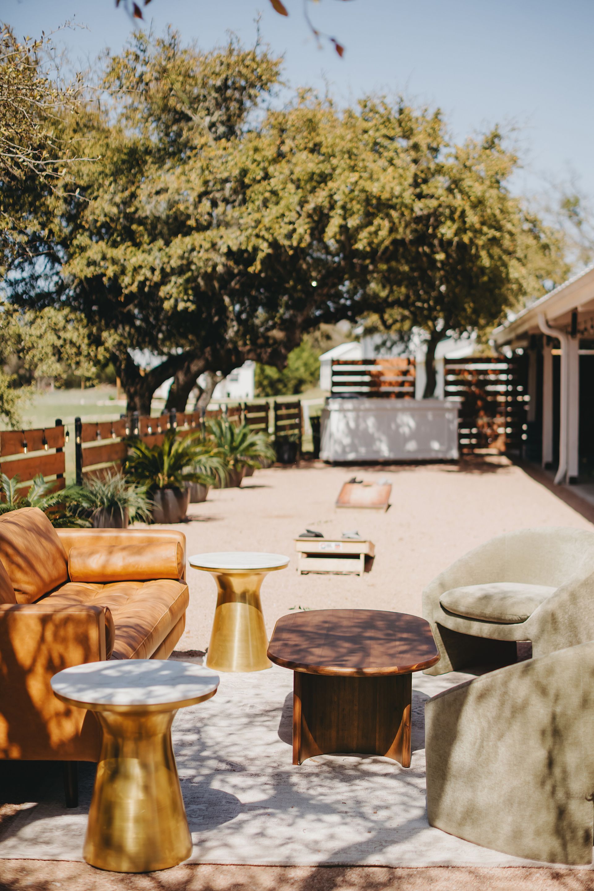 Outdoor lounge area with tan leather couch, plush armchairs, gold side tables, and a wooden coffee table on a patio.