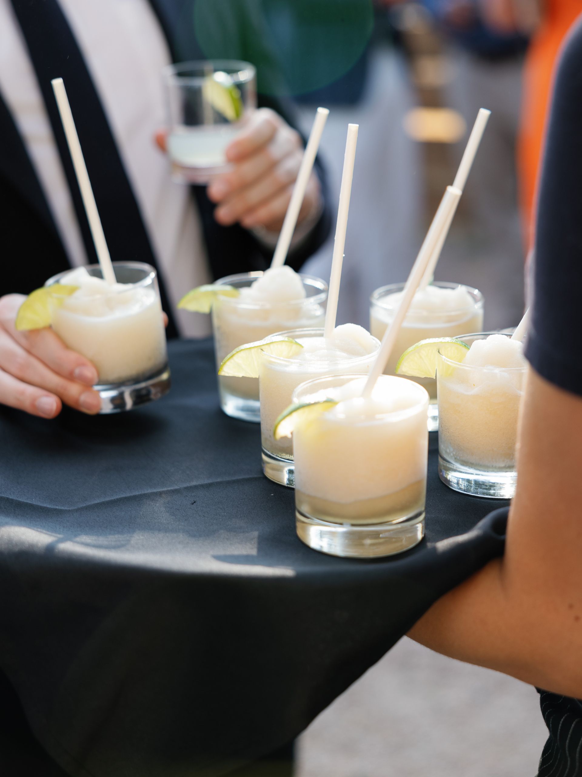 A server holds a tray of glasses filled with frozen, lime-garnished cocktails at an event.