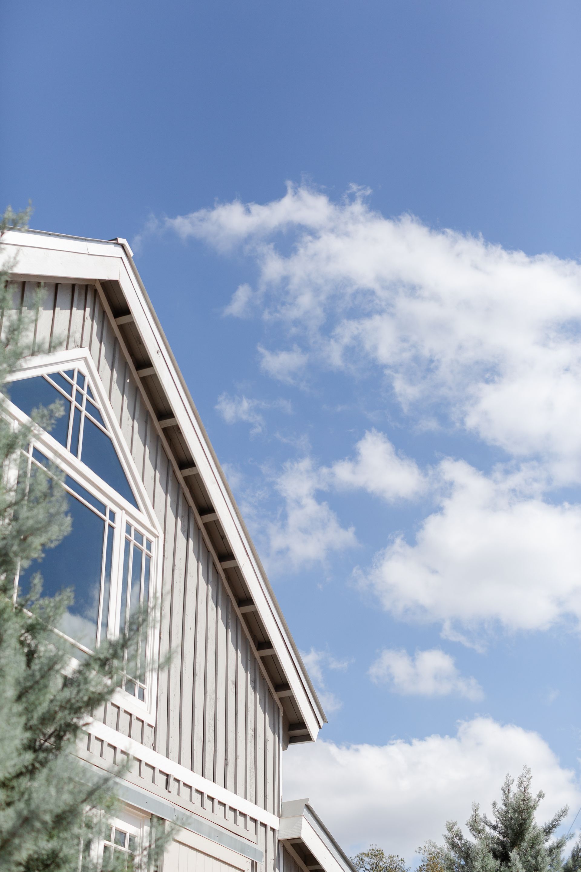 White building facade with large windows against a bright blue sky and scattered clouds