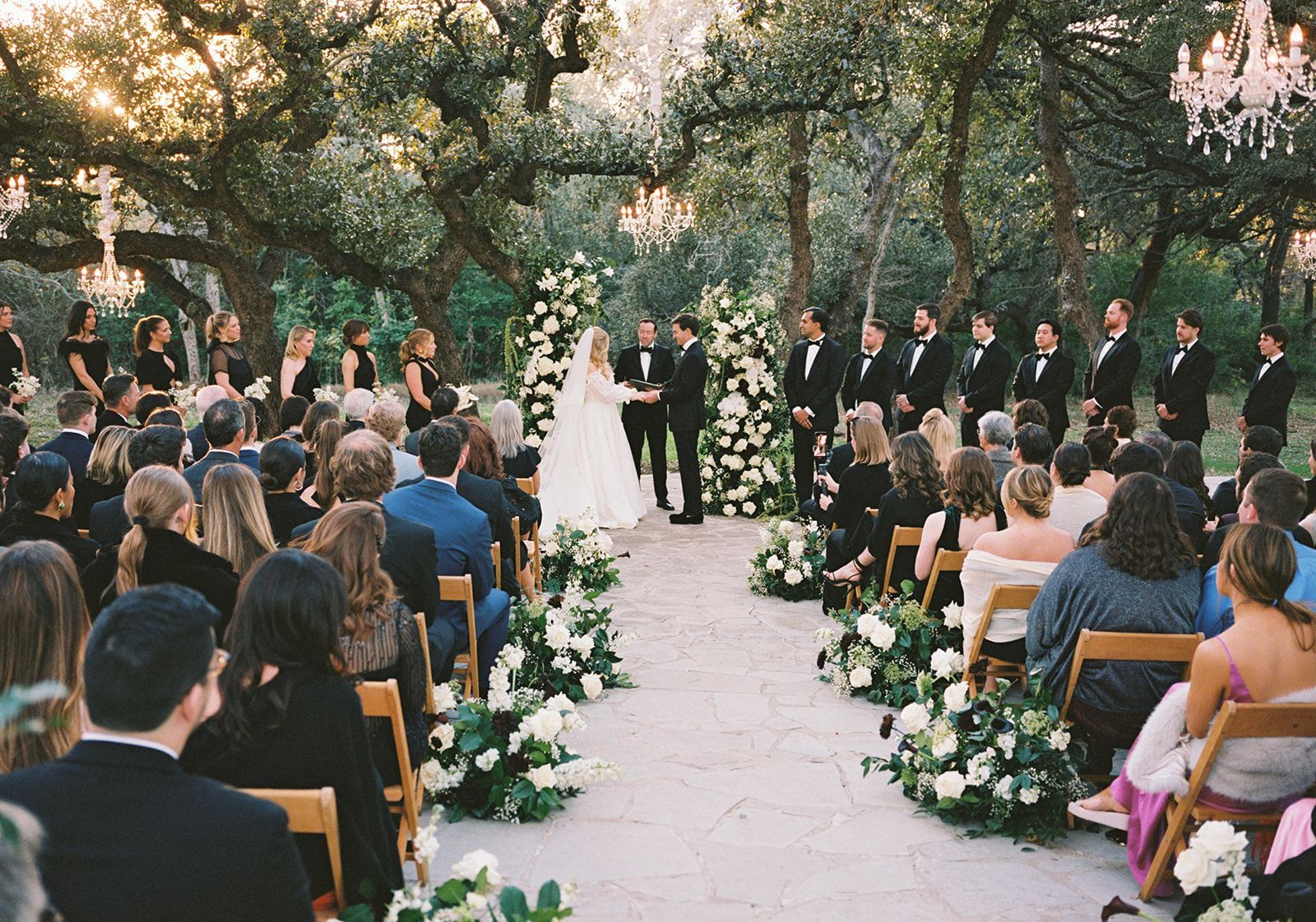 An outdoor wedding ceremony in a forest setting with a bride and groom at the altar and guests seated in rows.