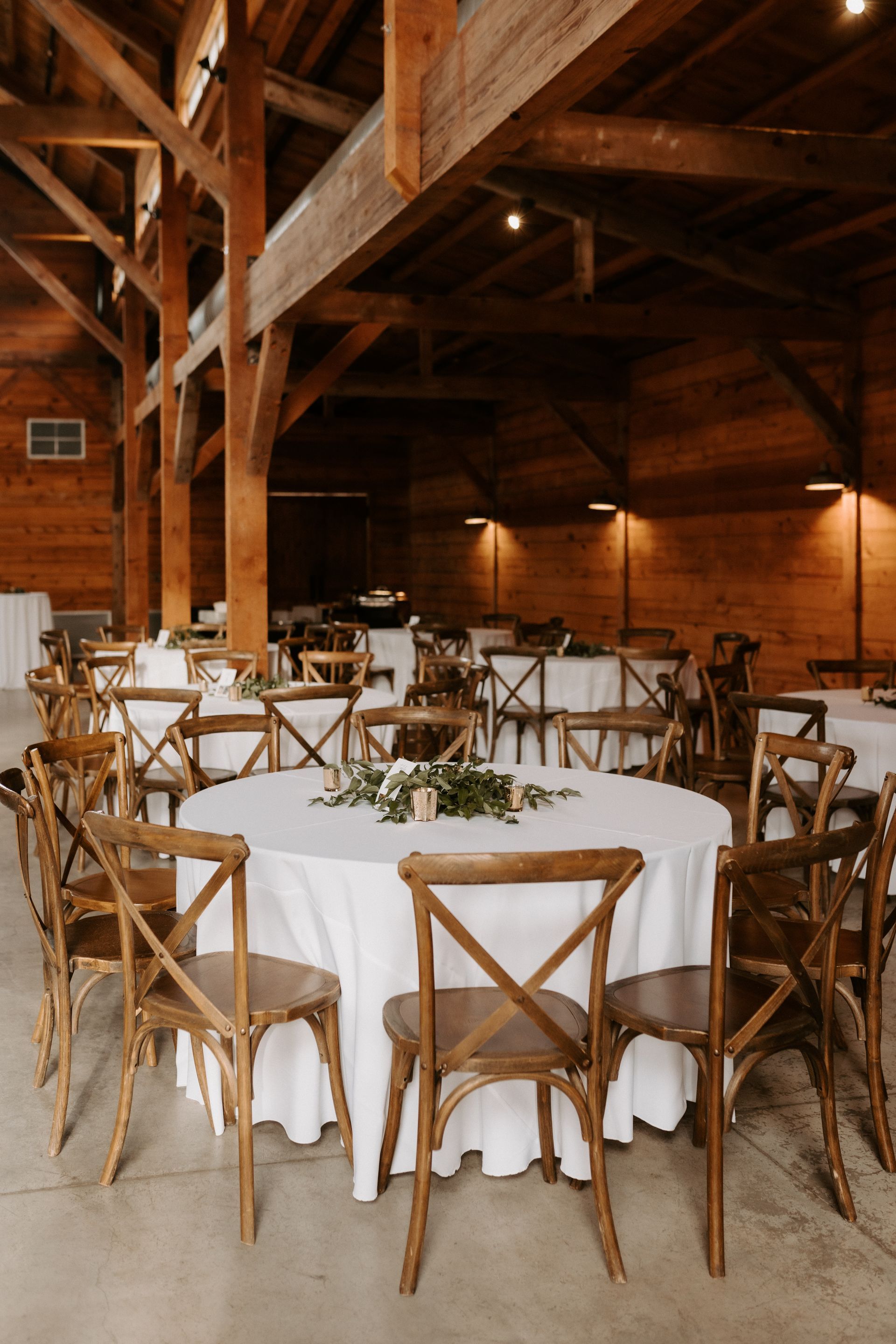 Round tables with white tablecloths and rustic wooden cross-back chairs inside Addison Grove's warm, wooden-beamed barn.