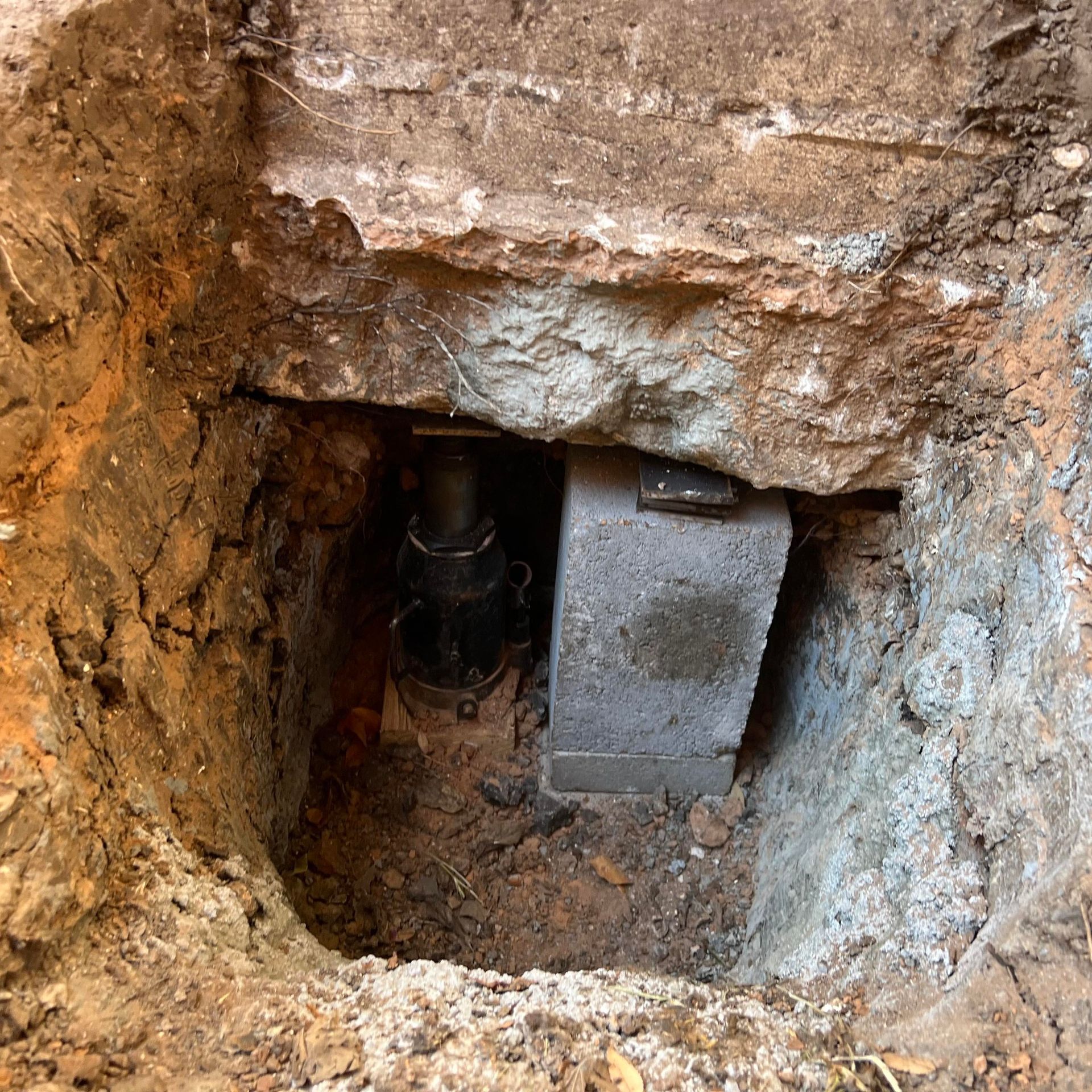 Exposed underground pipe and concrete block in a rough dirt excavation pit