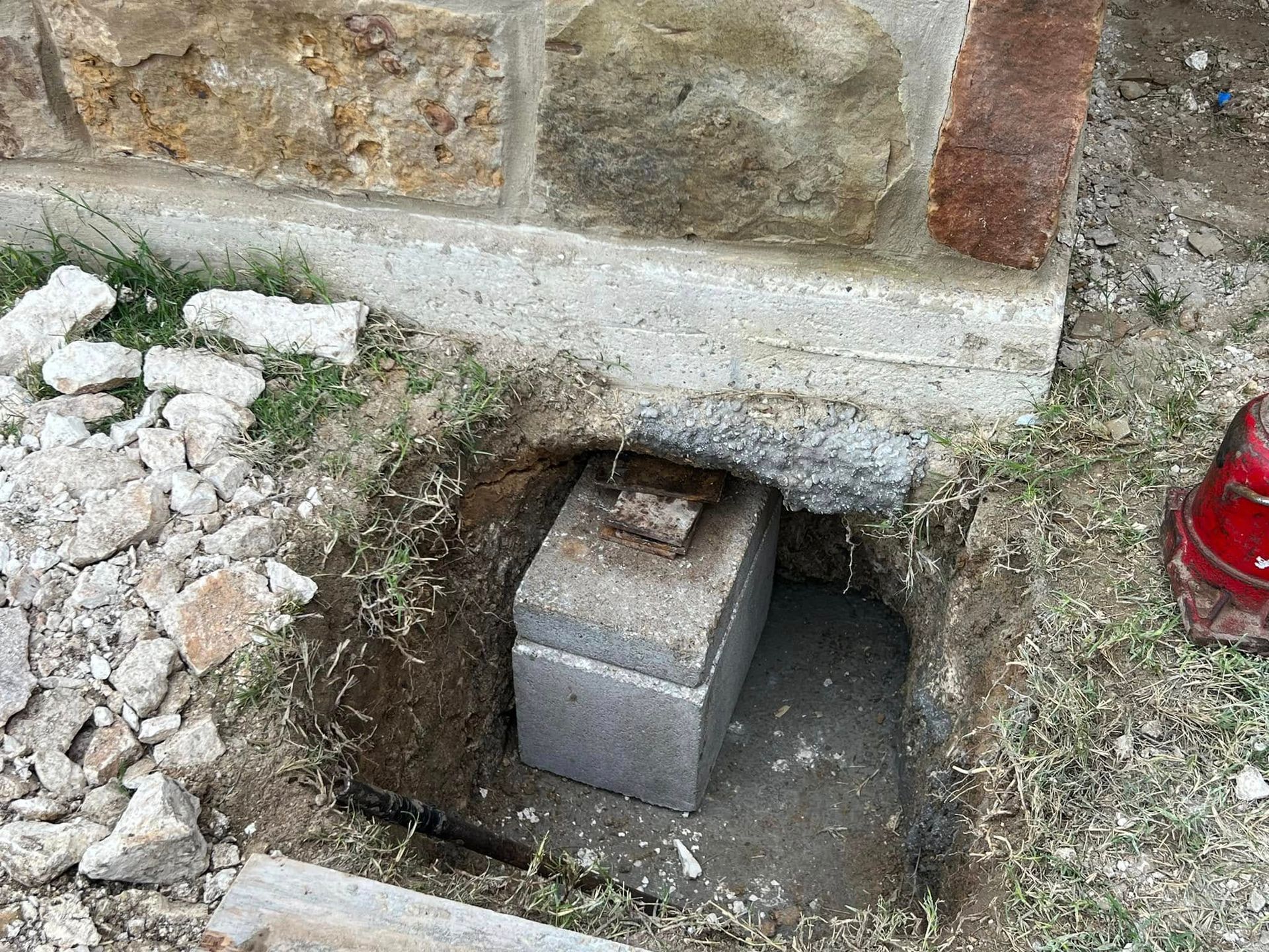 Open hole in stone wall base with a concrete block inside, beside rubble and a red fire extinguisher