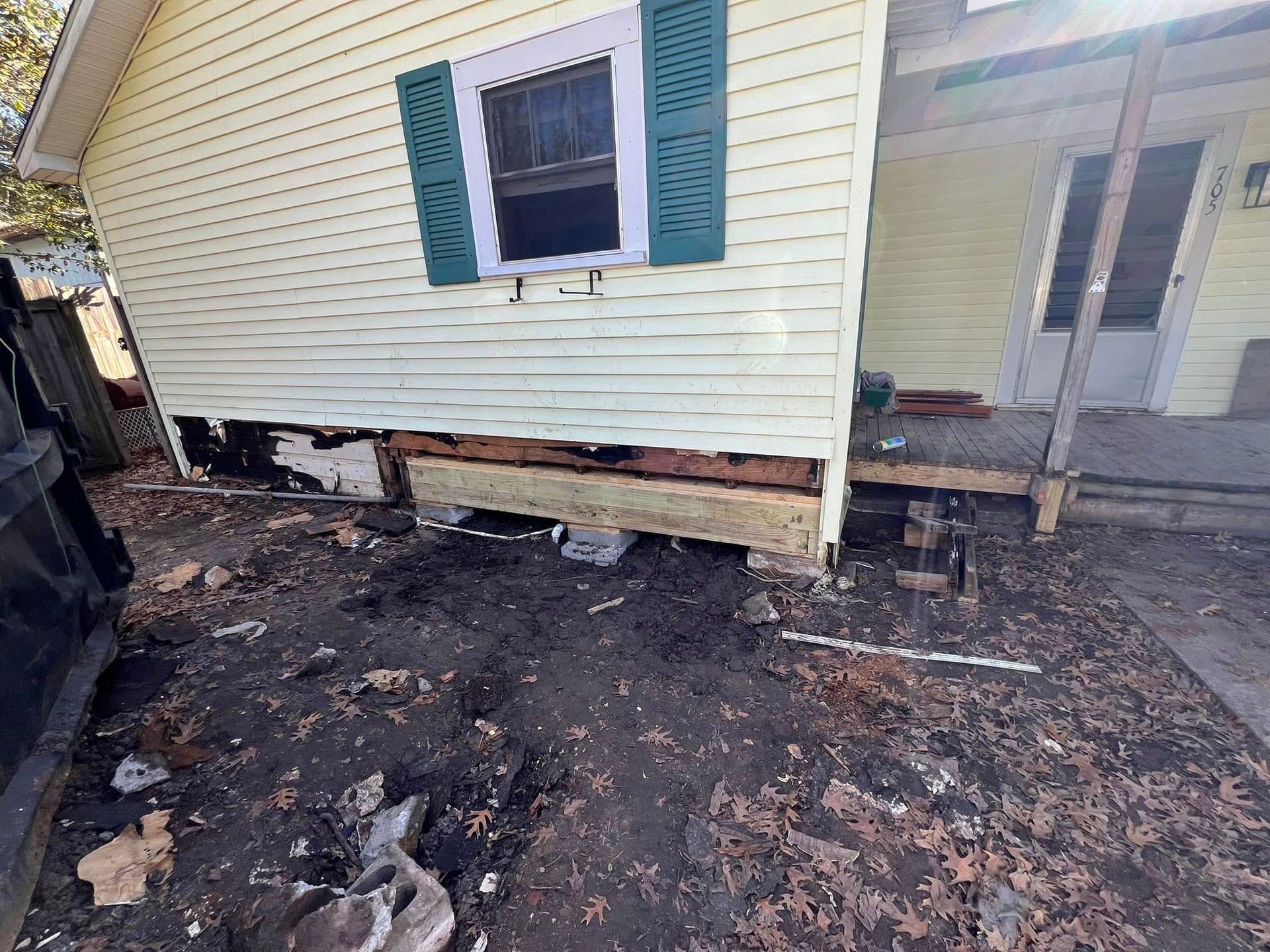 Damaged house exterior with burned ground and broken siding beneath a window and porch.