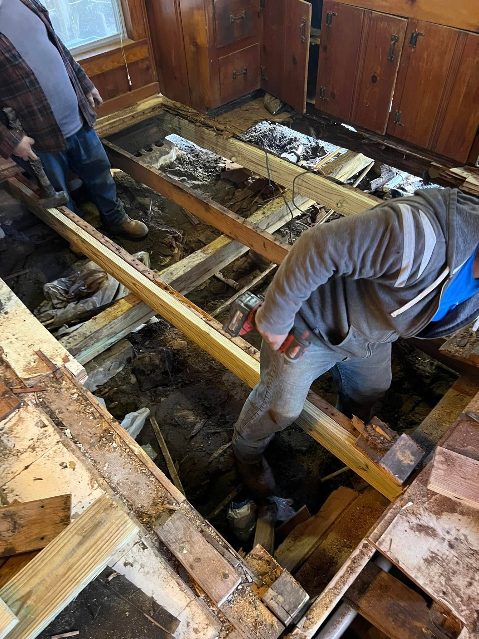 Workers repairing a damaged wooden floor with exposed joists in a room