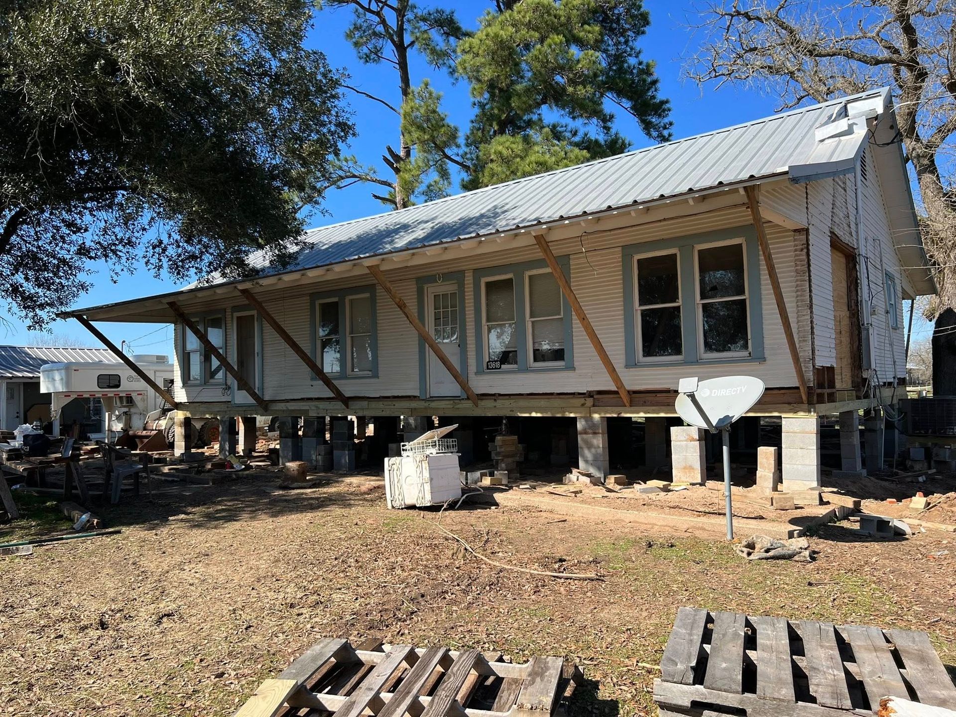 Raised house under construction on stilts, with metal roof, wooden framing, and debris in a yard.