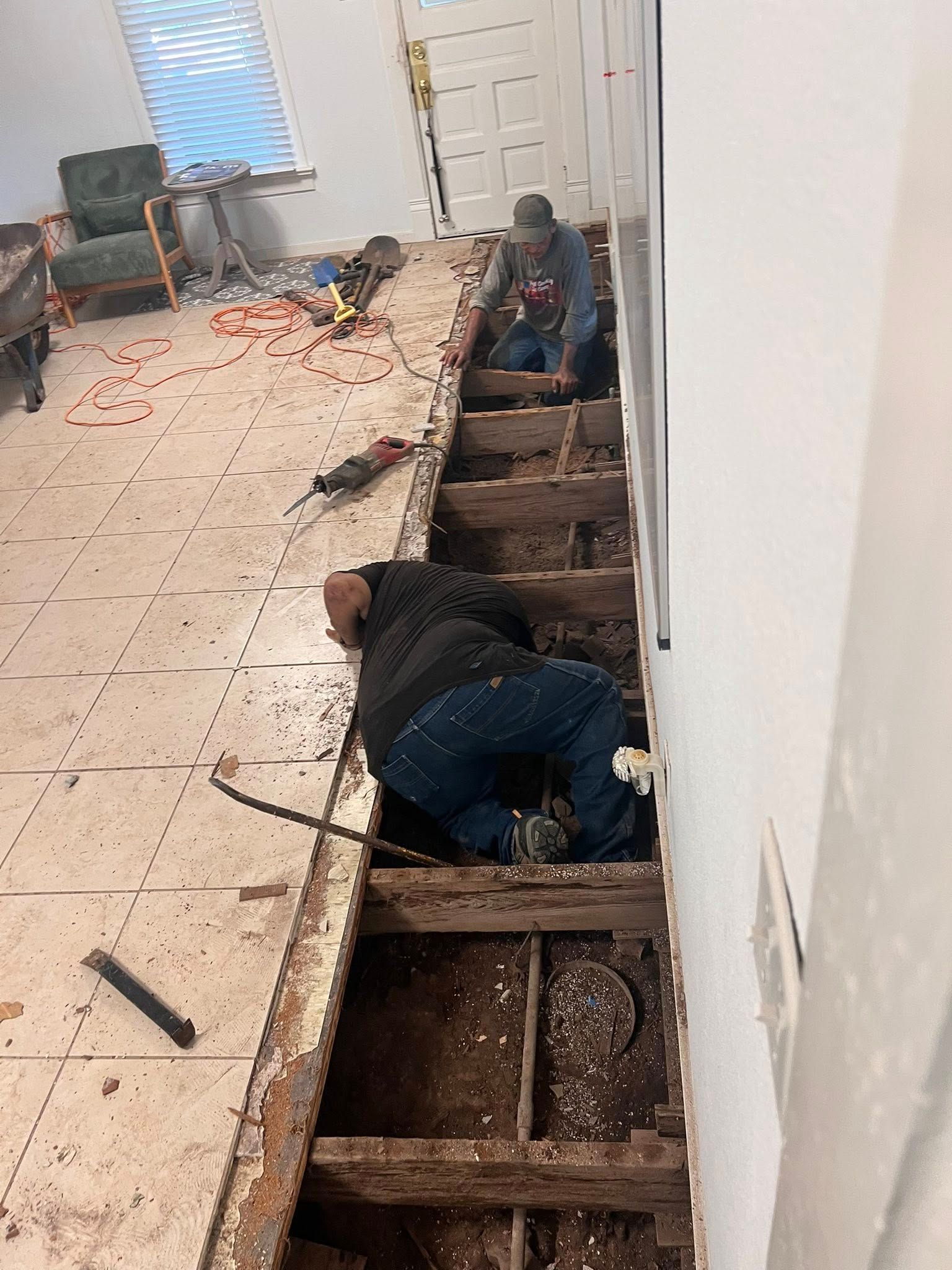Workers removing floorboards in a hallway, exposing the subfloor and debris during renovation.