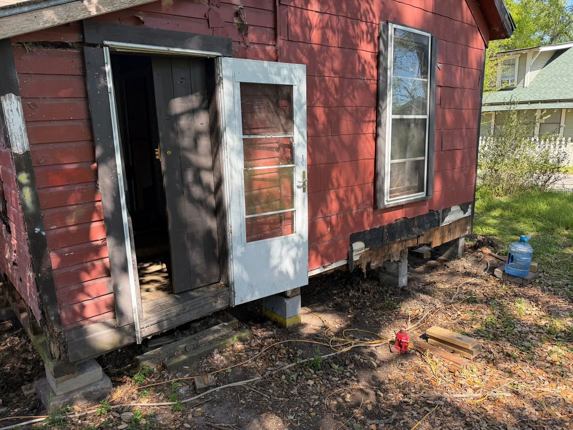 Red shed with open door and window, chicken standing in a dirt yard outside.