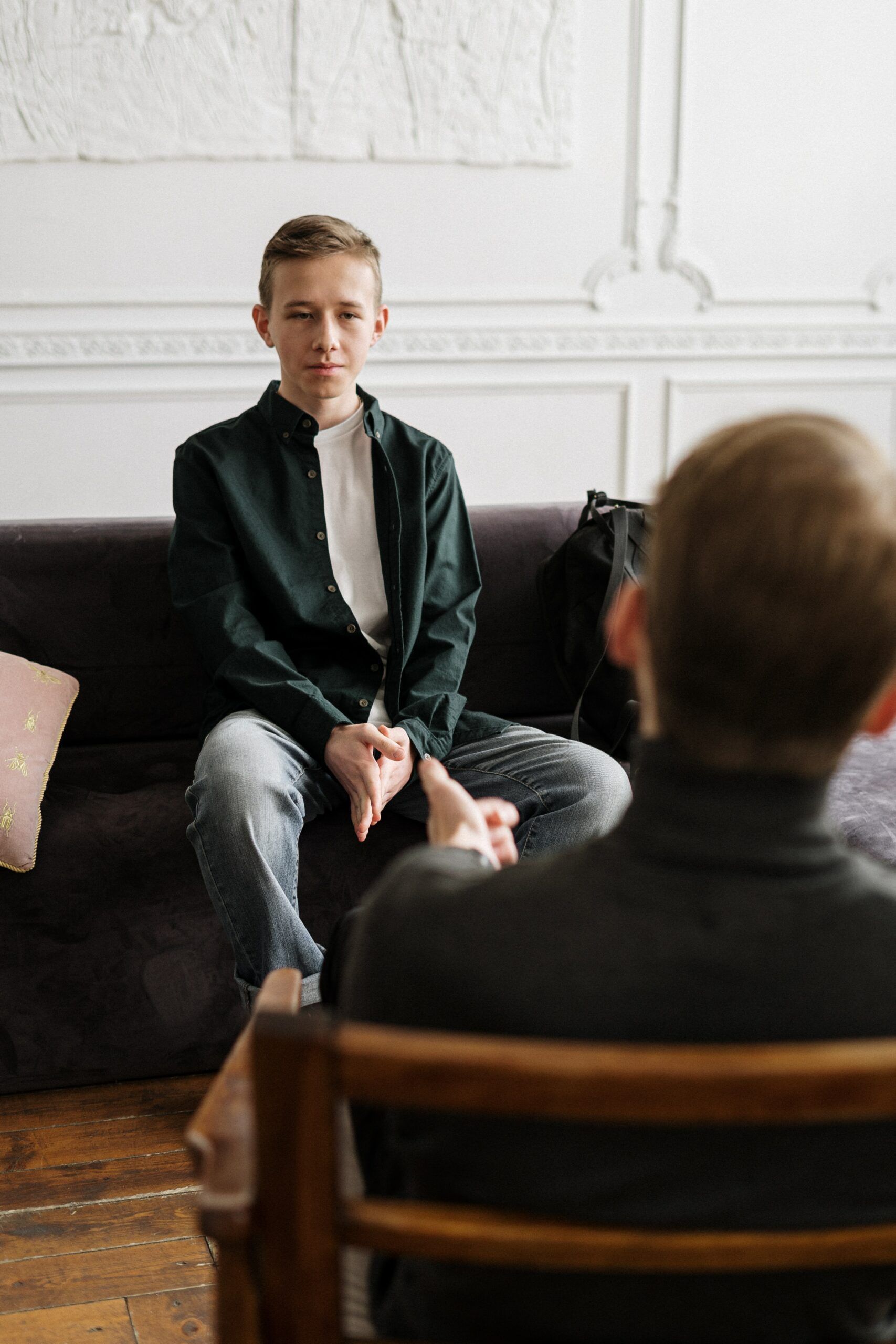 Two people in conversation in a bright room; one sits on a couch, facing a seated interviewer.