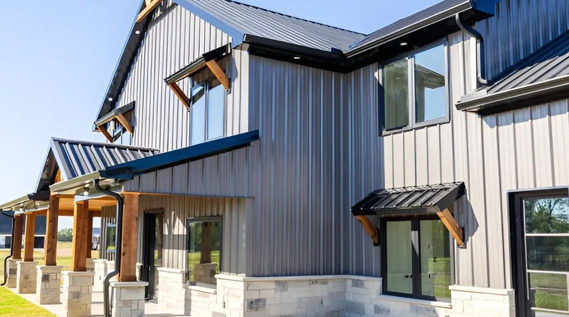 Modern home with grey metal siding, black trim, and wood accents under a bright sky.