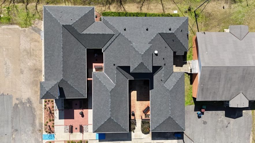 Aerial view of a large gray-roofed house with a driveway and surrounding yard.