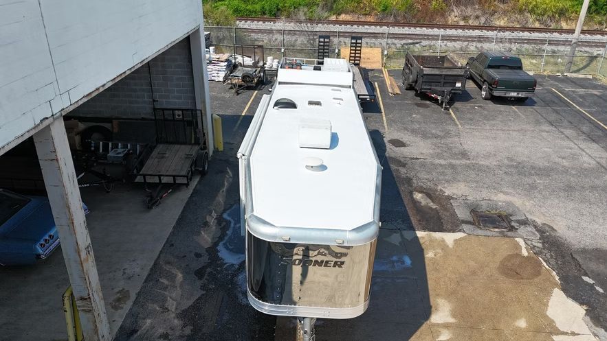White RV parked in a lot beside a building, with a covered area and other vehicles nearby.