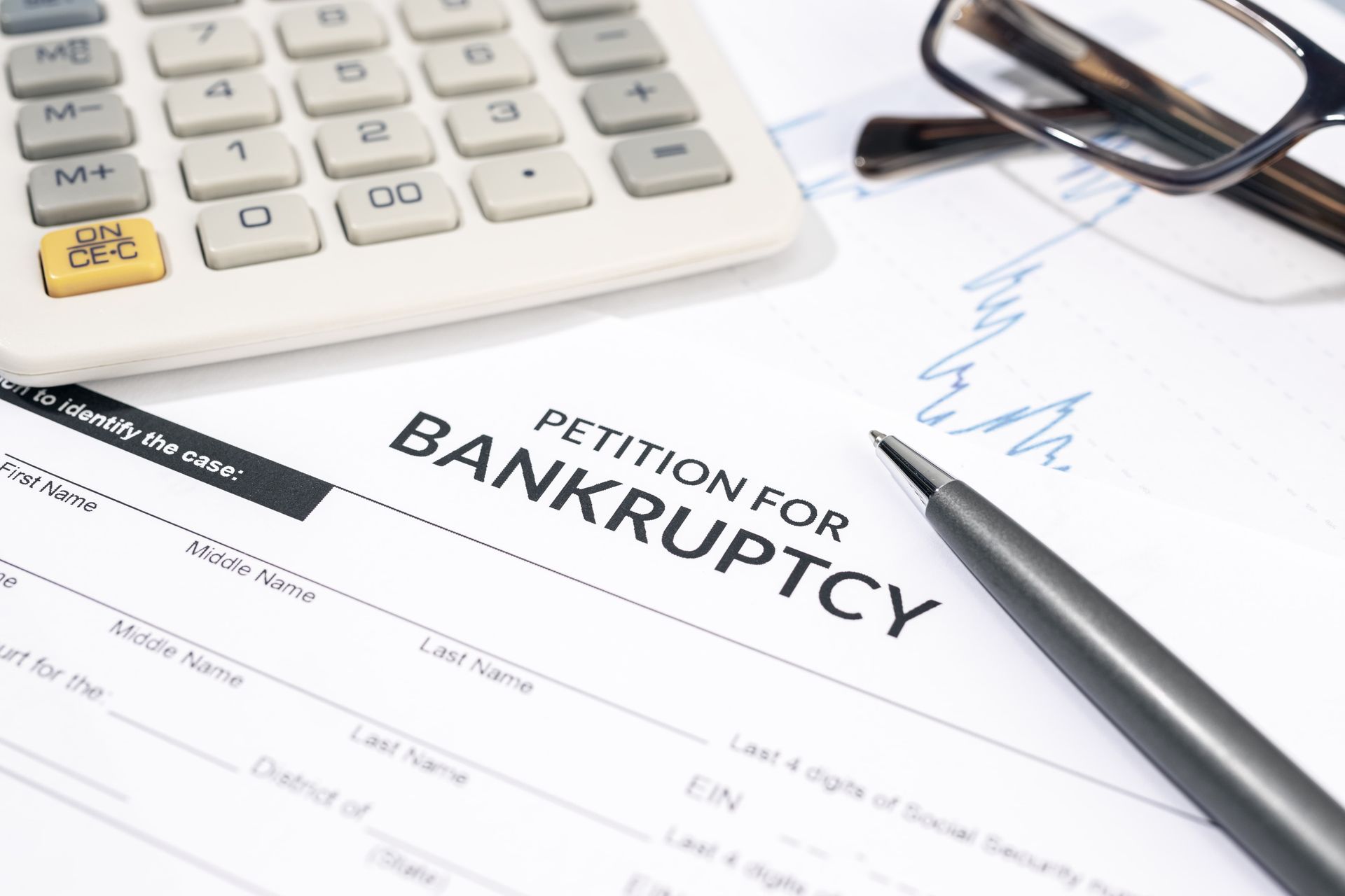 Bankruptcy petition form beside calculator, glasses, and pen on a desk