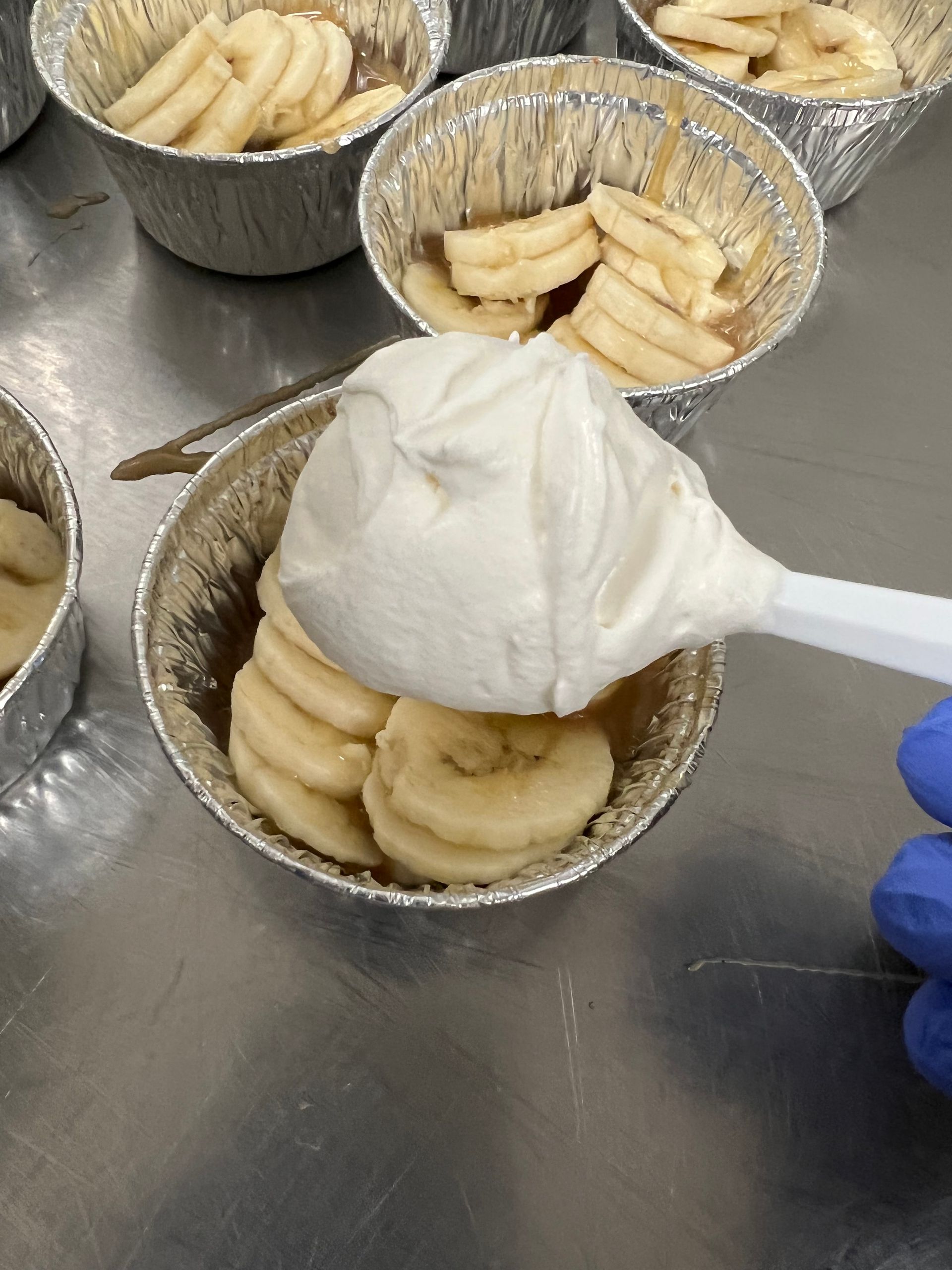 A person is pouring whipped cream into a bowl of bananas