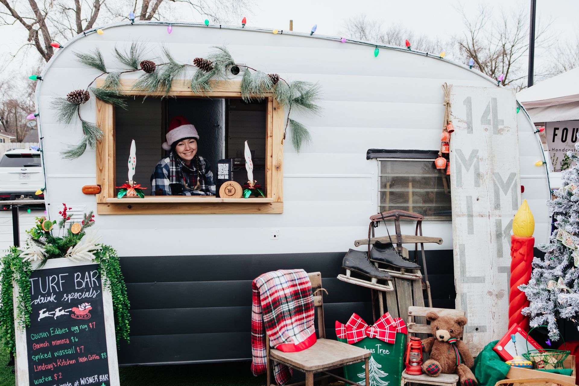 A woman in a santa hat is standing in front of a trailer decorated for christmas.