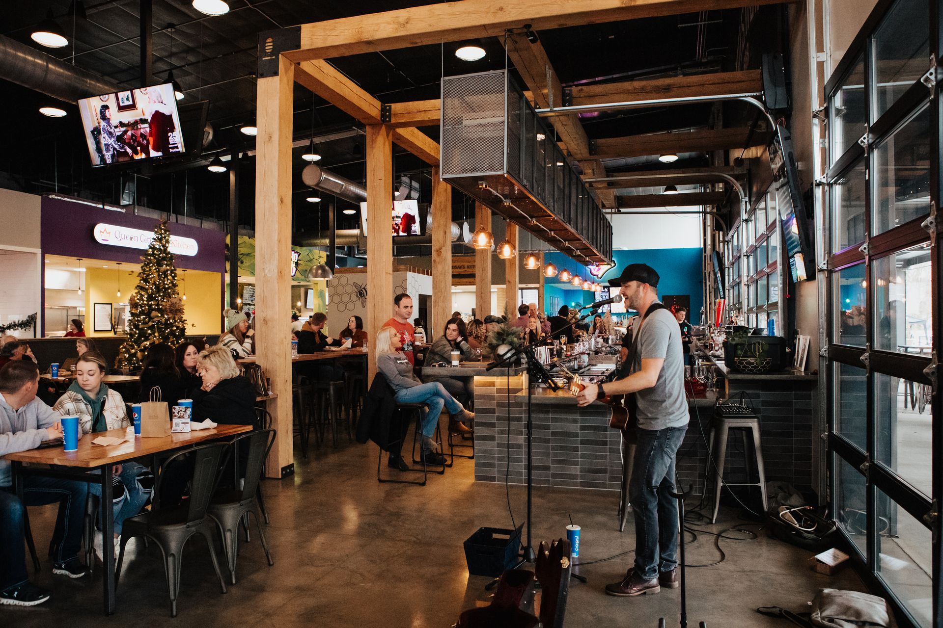 A man is playing a guitar in at 14 Mill Market while people sit at tables.