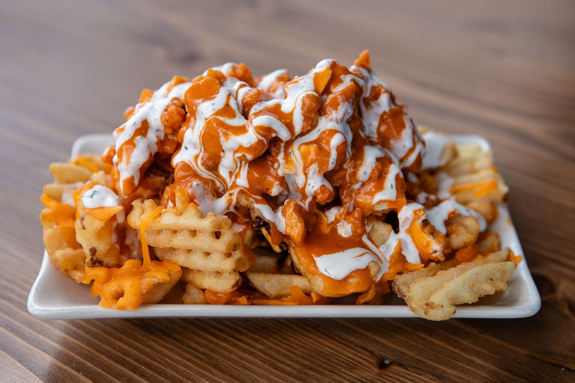A plate of waffle fries with chicken and sauce on a wooden table.