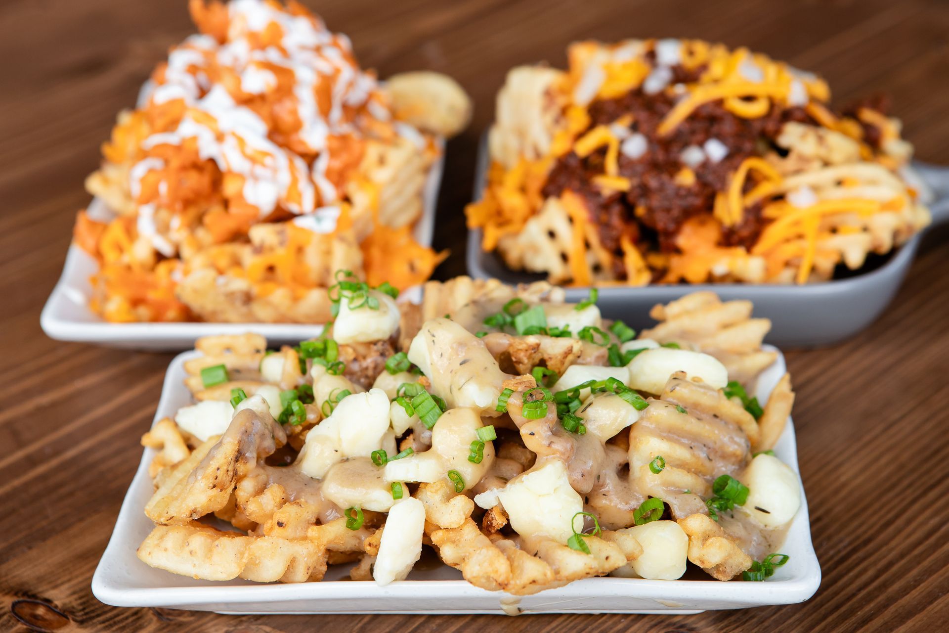 Three plates of french fries are sitting on a wooden table.