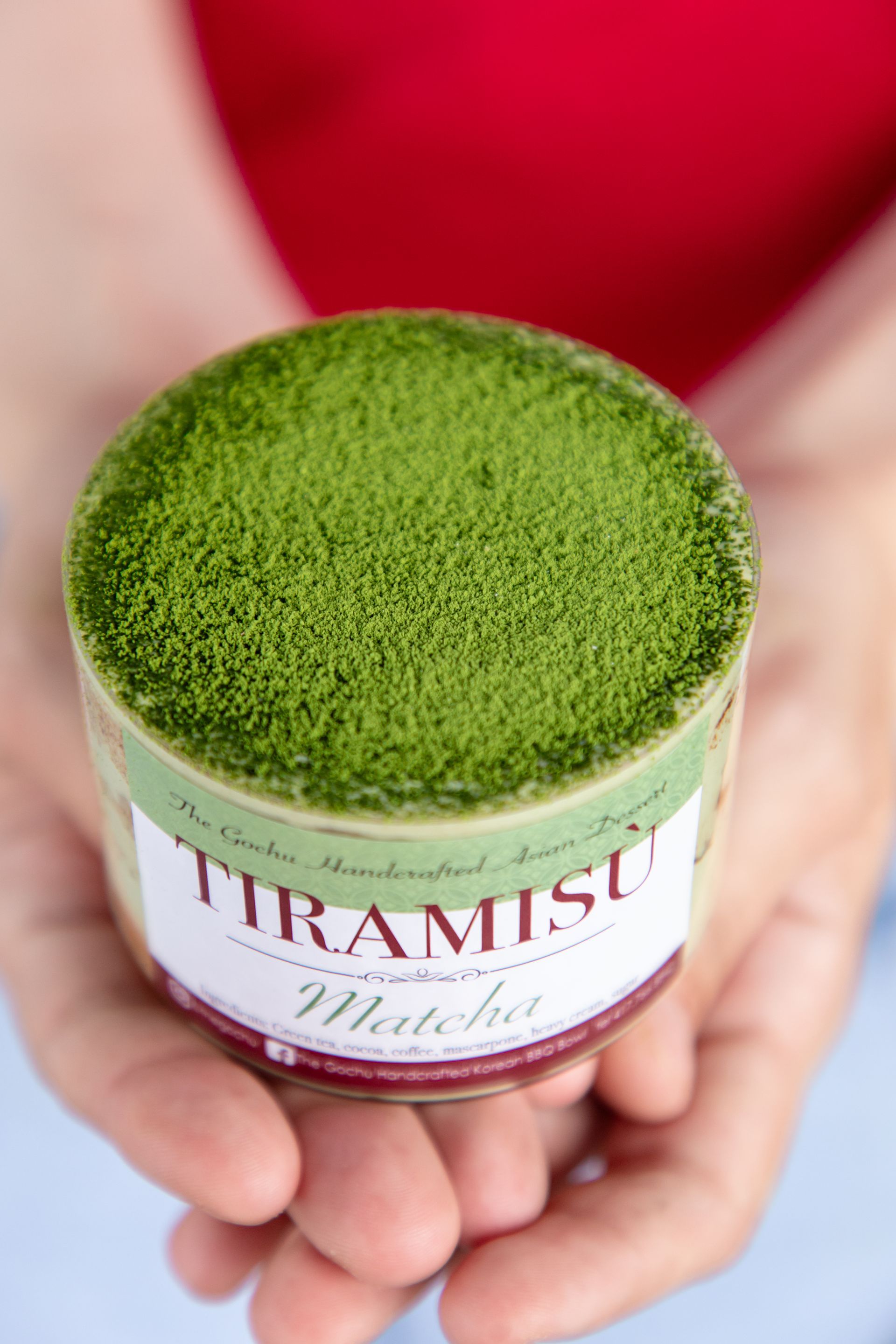 A person is holding a cup of tiramisu with green powder on top.