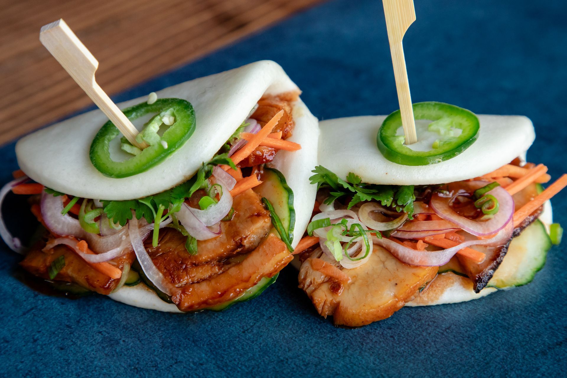 Two bao buns with meat and vegetables on toothpicks on a blue plate.